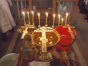 Церковные свечи рядом с чашей святой воды и крестом